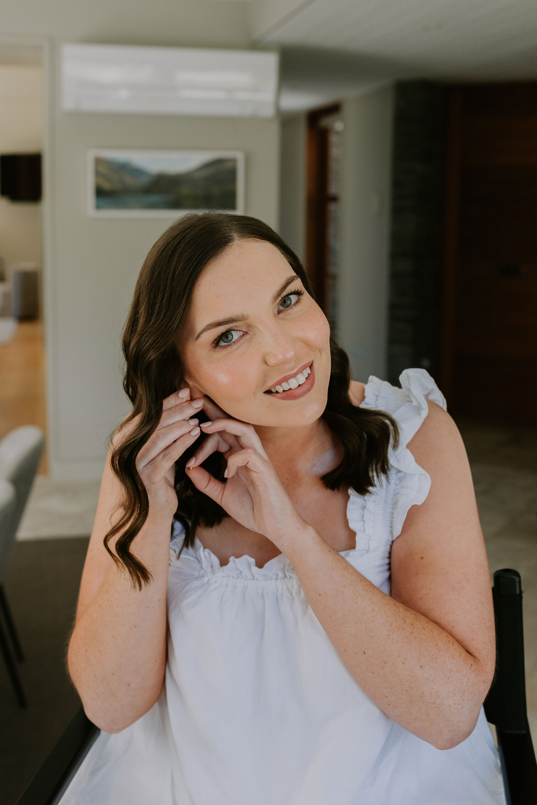 bride with hair and makeup done for wedding putting jewellery on